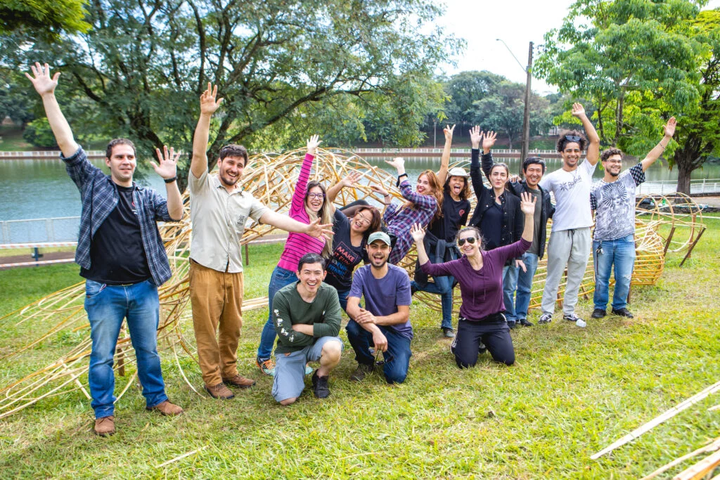 Grupo de bambuseiros posando em frente a escultura "Morada" construída em bambu